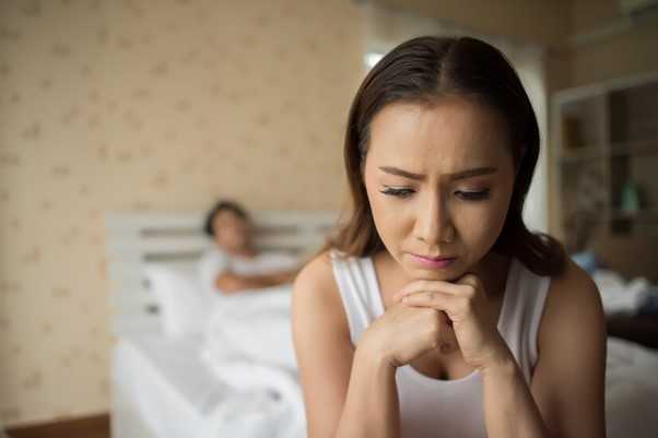 Woman sitting on the edge of the bed while a man lays in the background