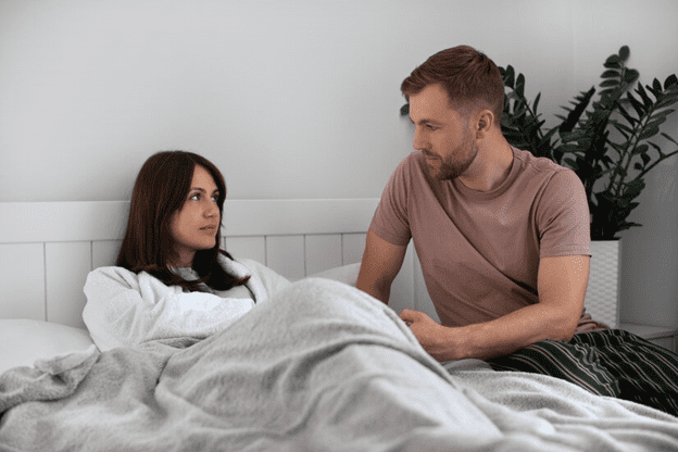 Female laying in bed while male sits on the edge of the bed