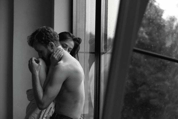 Couple holding each other against a window pane